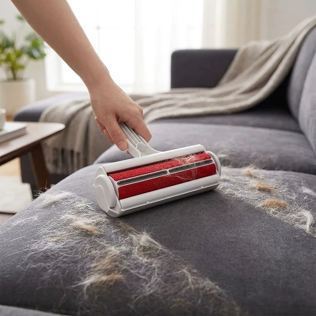 Person using a red roller brush to clean a gray sofa with pet hair collected on it.